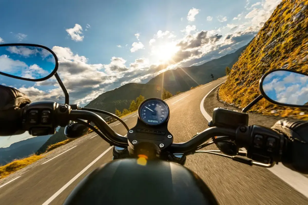 A person riding a black motorcycle on a mountain road on a sunny day. 